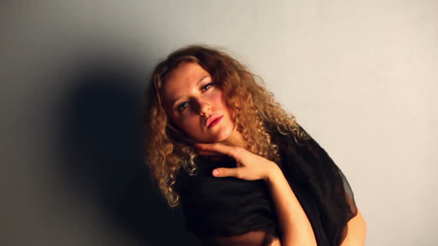 Young model with curly hair poses wrapped in black shawl and casts shadow on wall