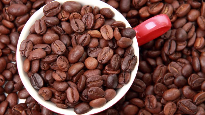 Textured background of dark coffee beans and white and red ceramic cup full of coffee beans