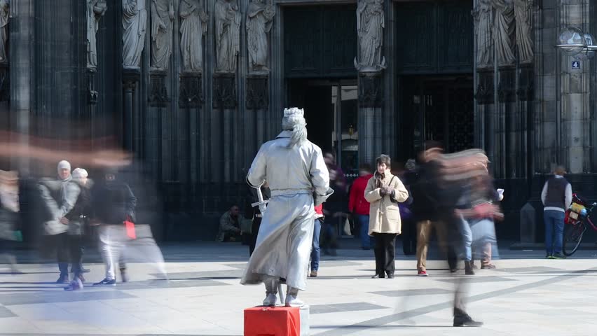 Cologne, Germany - March 31 2013: Timelapse shot of a performance artist dressed as a knight posing in front of Cologne Cathedral in Cologne, Germany. Pedestrians rush by.