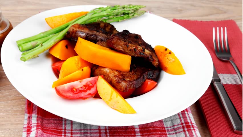 meat food : rare medium roast beef fillet with mango tomatoes and asparagus served on white dish on red table map over wooden table