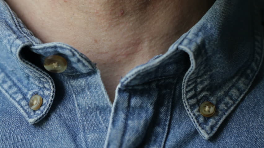 Close shot of hands doing up the collar of a denim shirt, and then undoing the shirt to reveal a green T-shirt underneath. Recorded with macro lens and very shallow depth of field.