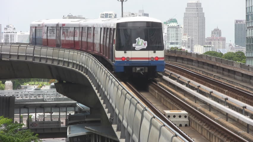 Bangkok, Thailand - circa 2012: A sky train passes and then bears left going away from the camera. A city scape of mainly tall buildings makes up the background. Traffic and pedestrians pass below.