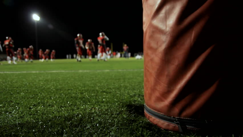 Dolly behind a goalpost as football players warm up before a night time game.