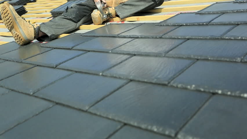Roof tiler installing slate tiles on property roof