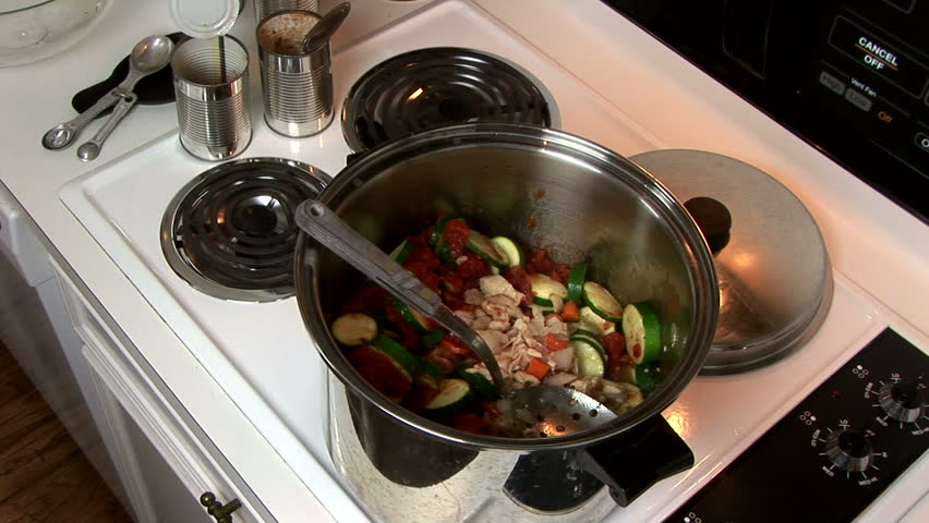 A woman in her kitchen stirring a large pot of hearty chicken vegetable soup.