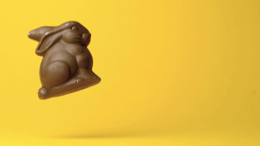 Chocolate bunny falling and rolling away against yellow background in slow motion