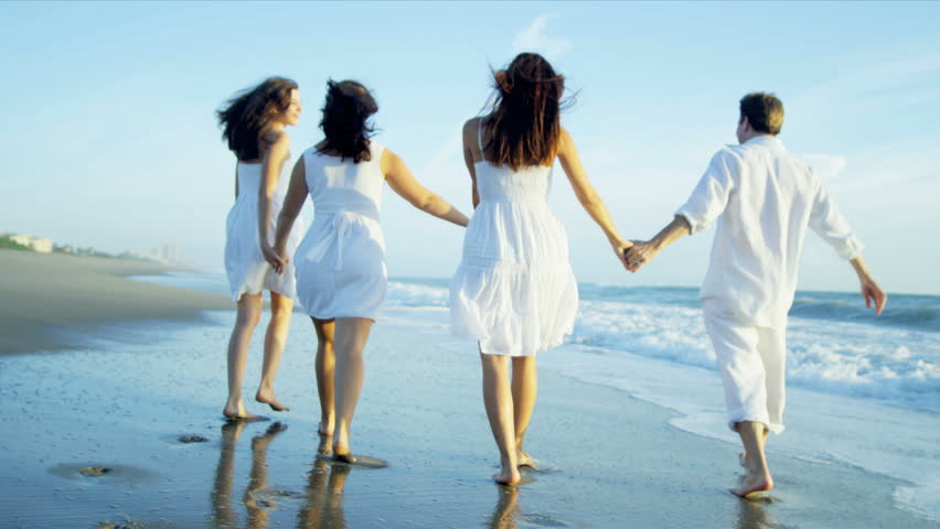 Happy Caucasian parents with teenage daughters enjoying time together walking through beach shallows shot on RED EPIC