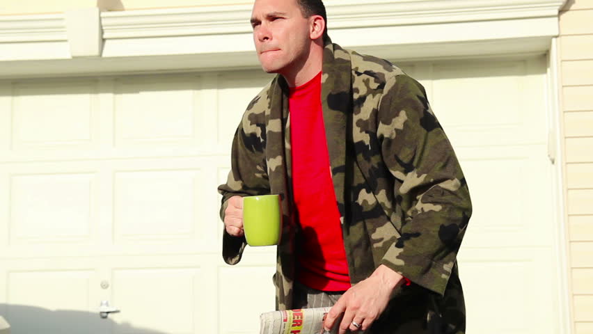 A man in his robe awaits for his daily paper on the driveway.