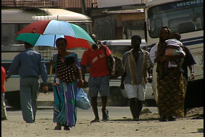 DAR ES SALAAM, TANZANIA - DECEMBER 1, 1998: Small group of people walking towards camera. A woman with a baby is carrying a huge umbrella.