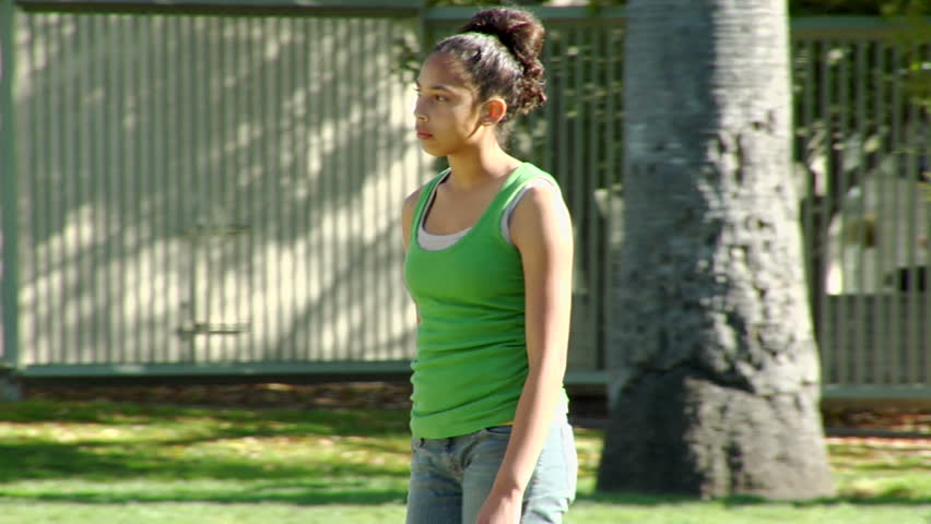 ootage of young ethnic teenage girl walking in park passing by water fountain and pondering in sad depressed about something that is making her feel uncomfortable.