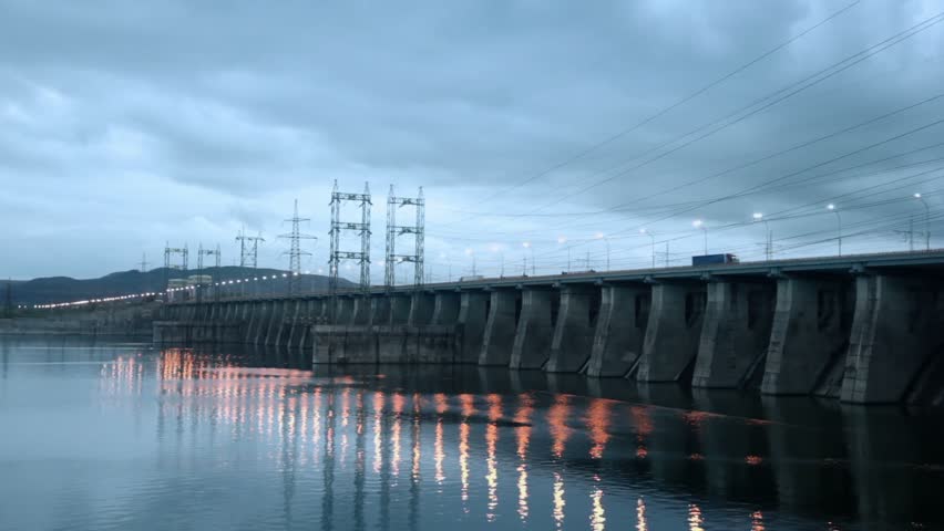 Traffic at dam of Hydroelectric power station on river at evening, pillars with high-voltage wires