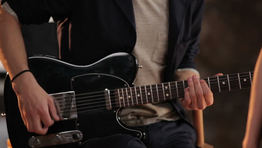 Charismatic girl singing in the studio accompanied by two guitarists