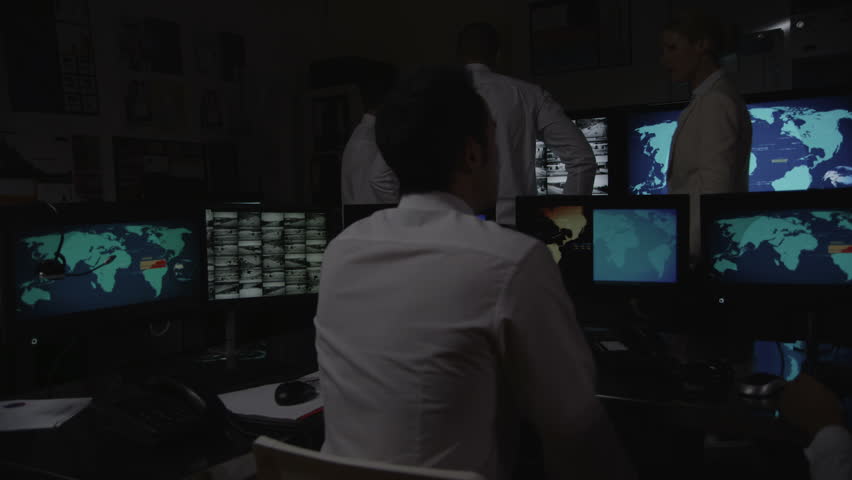A team of security personnel working in a busy system control room, could be a weather station/airport traffic control. It could be a  power station or police/army control facility. 
