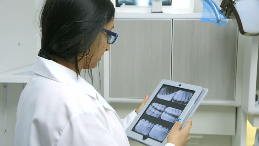 A young female dentist or intern reviewing dental x-rays on an electronic table turns and smiles