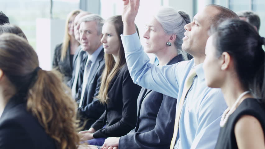 A multi ethnic group of business people of mixed ages are listening to a presentation at a business seminar and asking questions. In slow motion. 