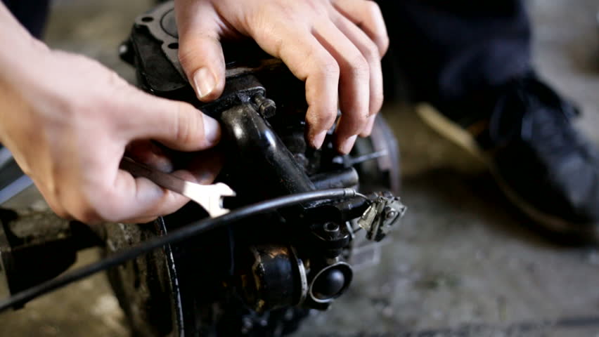 Young man cleaning a dirty engine of a mini motor. A lot of oil. Working in workshop on the floor. Unscrewing parts of the motor.