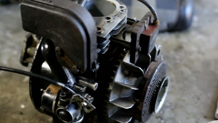 Young man cleaning a dirty engine of a mini motor. A lot of oil. Working in workshop on the floor. Unscrewing parts of the motor.