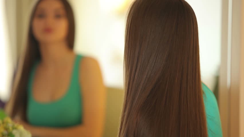Woman brushing hair and looking at camera with smile. close-up
