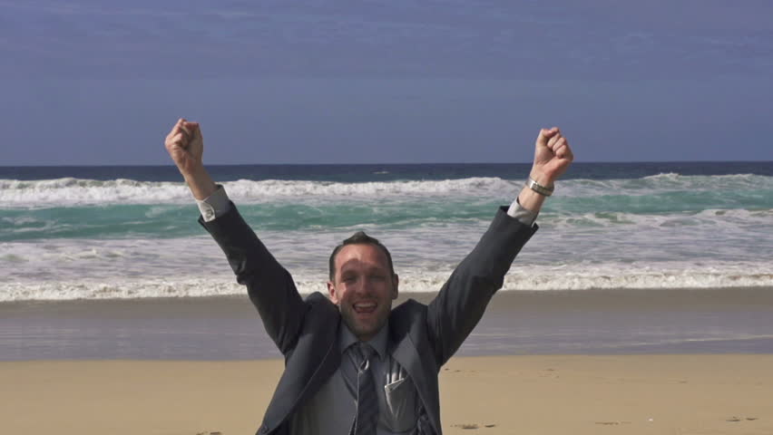 Excited businessman screaming by the sea and raising hands to the sky on beach
