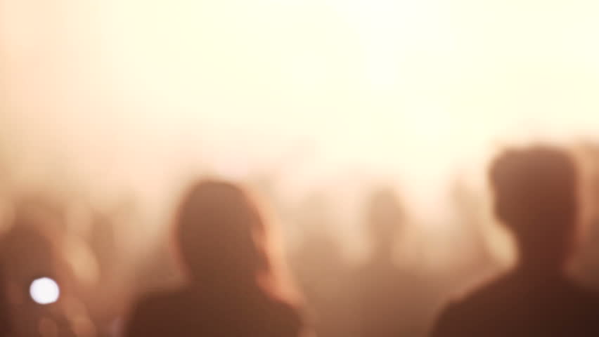 Big Music Show with a very excited crowd, rack focus on silhouetted people raising hands up with flashing lights. 