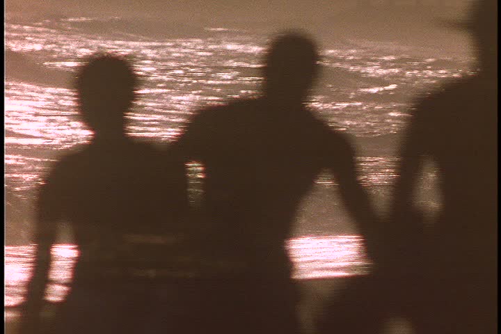 Slavery reenactment in Ghana, Africa. CU silhouettes of overseer leading five men in chains (two are boys) up beach in very bright sunlight. 