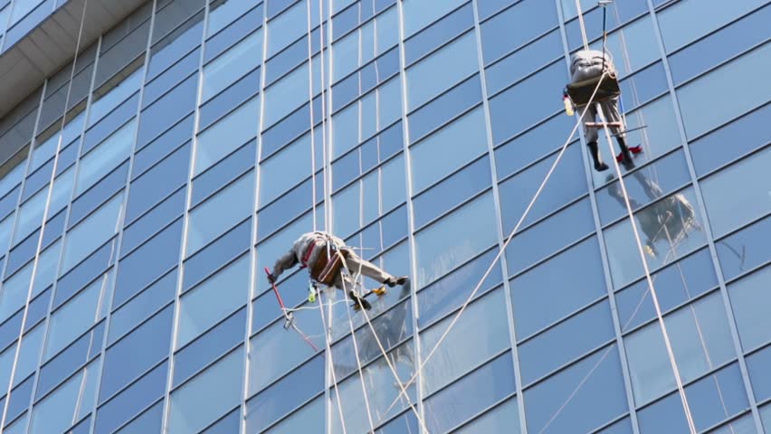 Two workers hang on ropes and wash windows of skyscraper, view from below