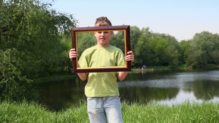 Boy in green t-shirt holds picture frame and moves it around his body behind back