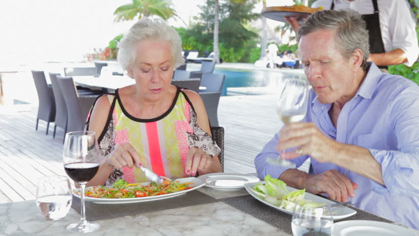 Waiter Serving Pizza To Senior Couple In Outdoor Restaurant
