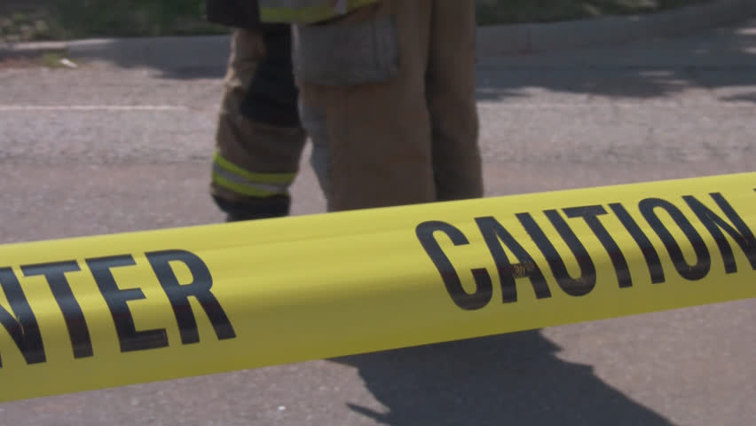 Fire fighters standing behind caution tape at emergency.