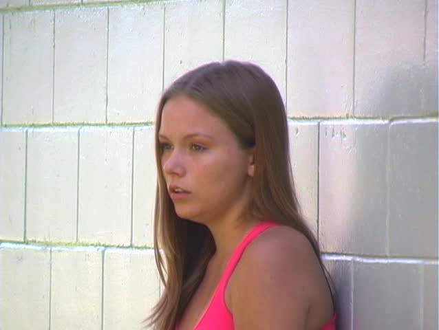 A lovely young blonde, leaning against a brick wall, is crying.
