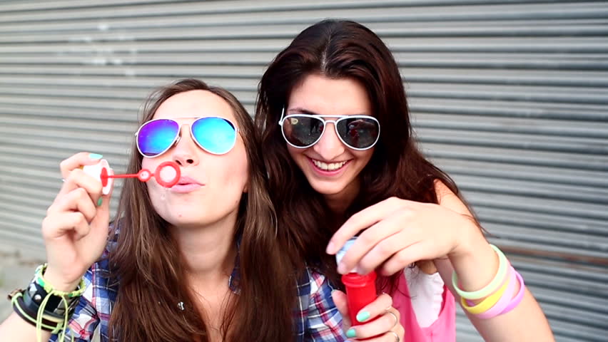 Cheerful hipster girls with sunglasses having fun making bubbles