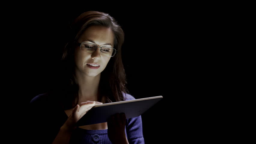 Attractive young woman using a tablet against a black background. 