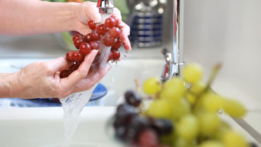 The camera focus moves from a woman washing a bunch of grapes to a bowl where she is placing the washed grapes.