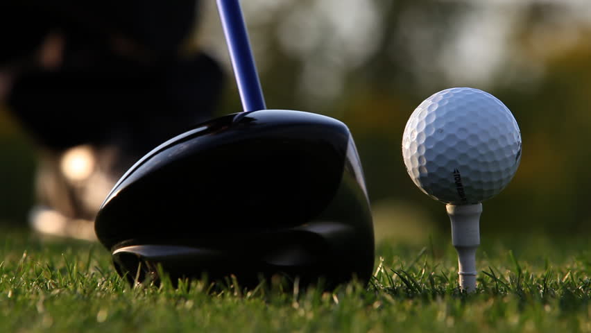 Close up of golf ball sitting on tee with driver swings and hits the ball