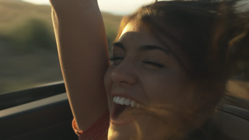 Happy Hispanic Teen Girl Rides In The Back Of Convertible, Raises Arm in The Air
