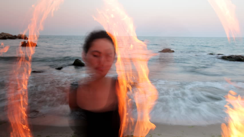 a woman does a fire performance on the beach