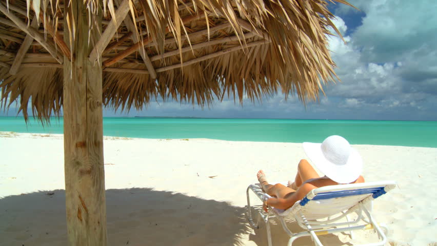 Elegant young female relaxing on a stunning white sandy beach looking at aquamarine waters