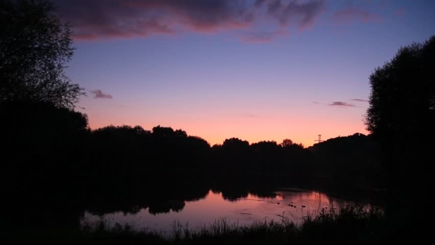 man with rucksack on bicycle looks at sunset lake 