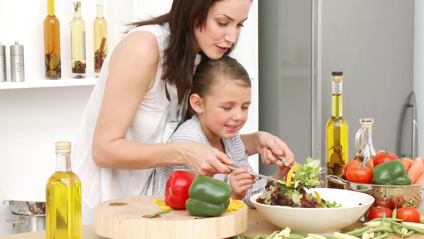 Beautiful mother and daughter preparing a salad in the kitchen. Concept of nutrition. Footage in high definition