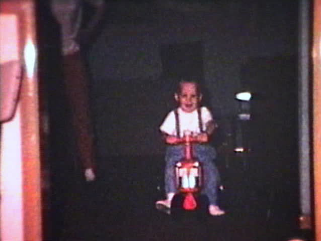A proud little boy rides his toy tractor around the house. (Vintage 8mm film)