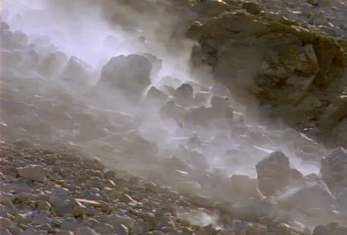 Boulders and smaller rocks roll and slide down a hill during a landslide.