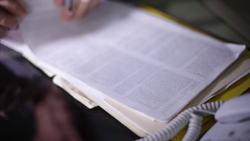 A man scanning through a legal document and making notes or signing various pages. Extremely shallow depth of field, pinpoint focus.