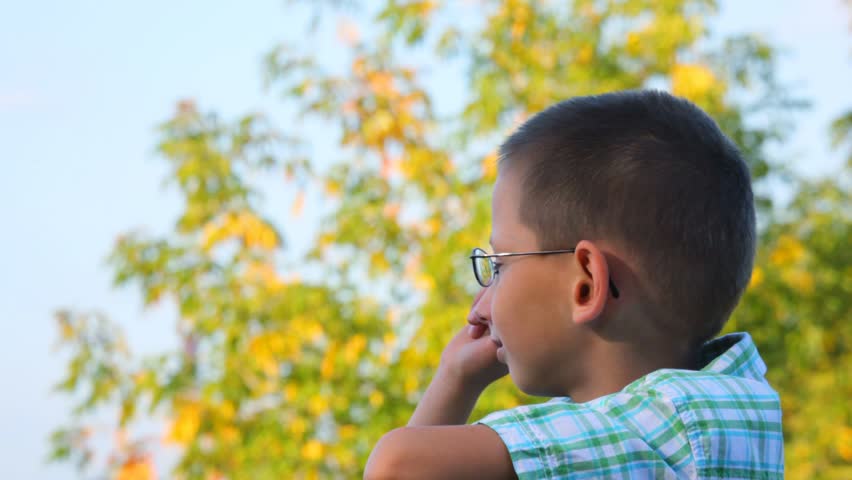 portrait of bespectacled boy jerkes his finger forward in park 