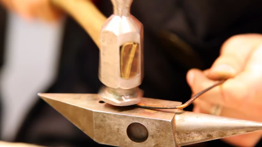 hammer knocks on heated slice of iron on an anvil, forming it 