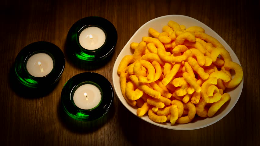 Stop motion showing a bowl of snacks being emptied. Shot against walnut background with flickering candles next to bowl.