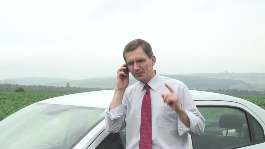 HD 1080i: Annoyed businessman talking on cell phone beside his car.