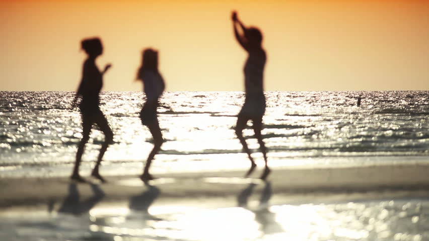 Three carefree girls dancing on the beach at sunset in silhouette