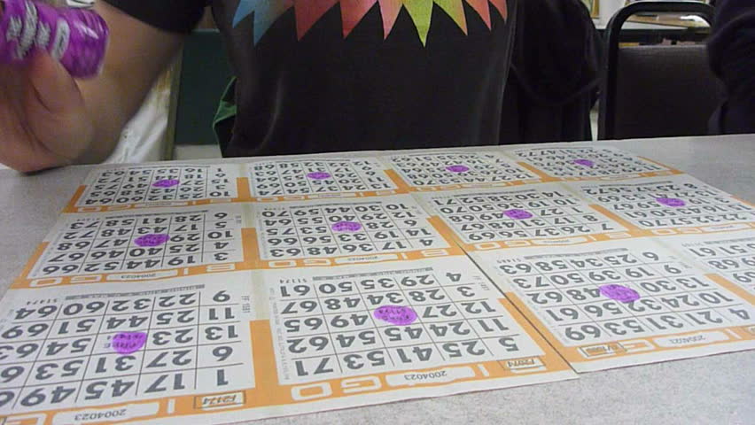 Woman wearing action shirt daubs ink on bingo cards in veteran bingo hall time lapse.