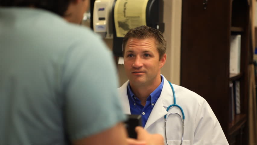 A relaxed,doctor talking sitting at a workstation in a clinic shares a laugh with coworkers.
