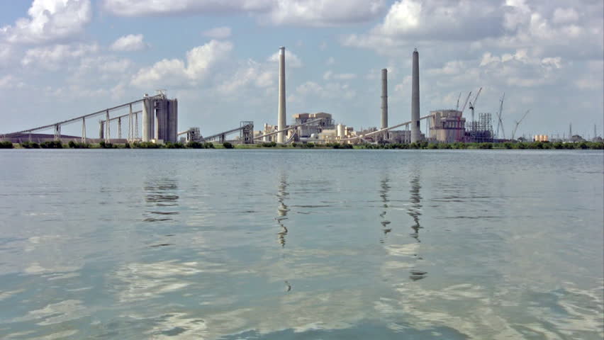 Video of a coal burning electricity generating facility plant. Towers and conveyor belts burning coal to make power. Pollution possible when operating. Lake with park used as water supply